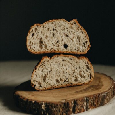 Appetizing halves of freshly baked sourdough bread served on wooden board on white table on black background in light studio