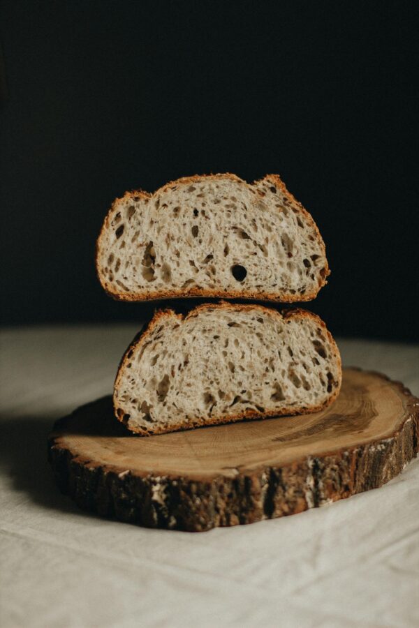 Appetizing halves of freshly baked sourdough bread served on wooden board on white table on black background in light studio